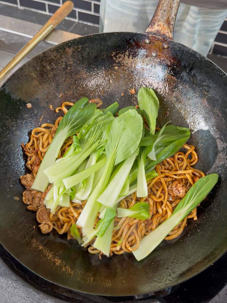 Adding fresh bok choy to Shanghai pork noodles in a wok