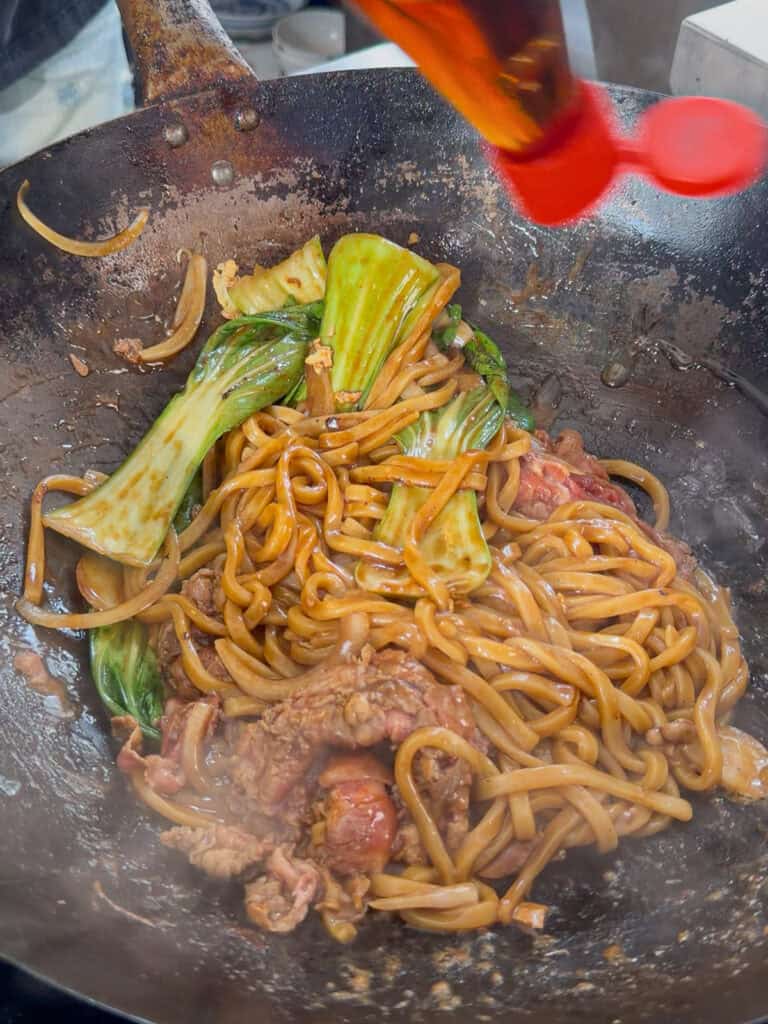 Beef cooking quickly with udon noodles in wok