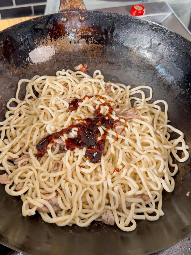 Cooked pork pieces mixed with Shanghai noodles in a wok-