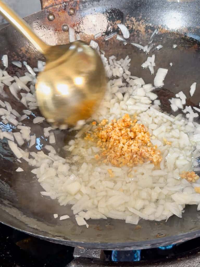 Cooking onion and garlic gently in a wok for Satay Beef Noodle sauce base