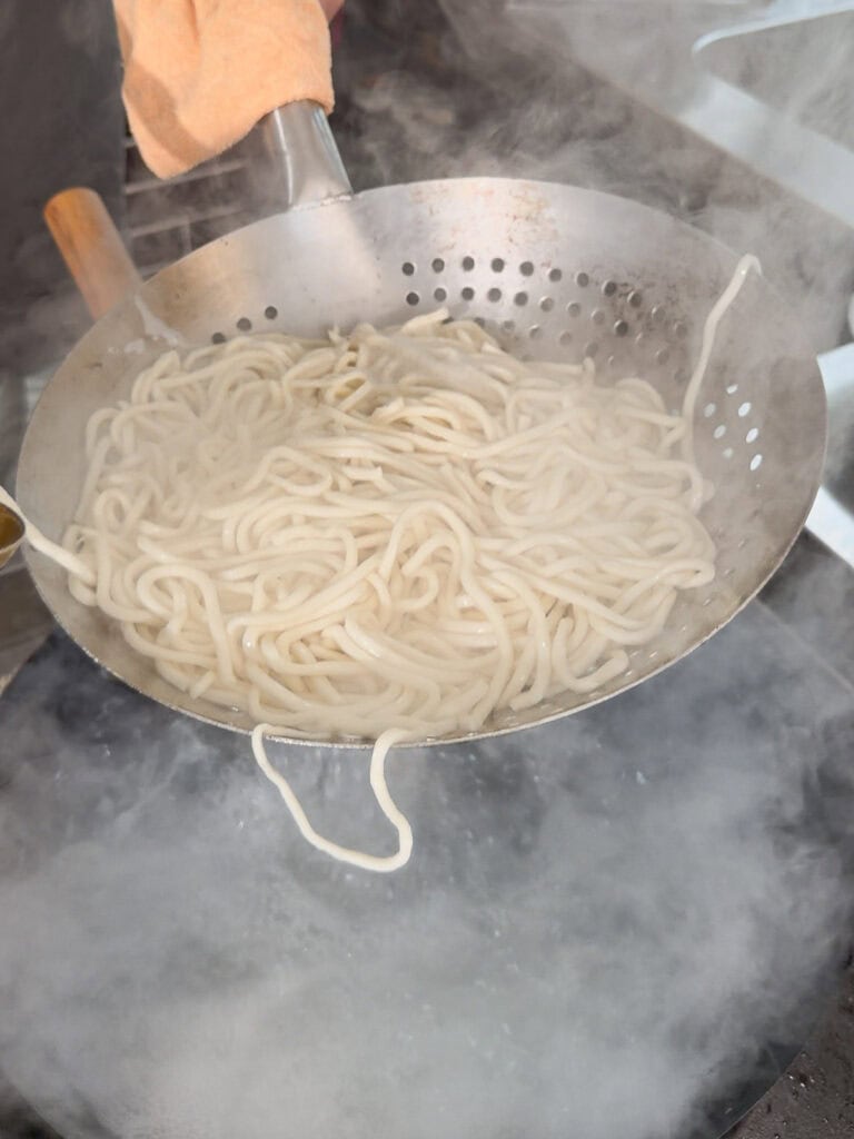 Draining cooked Shanghai noodles in a perforated strainer over a wok