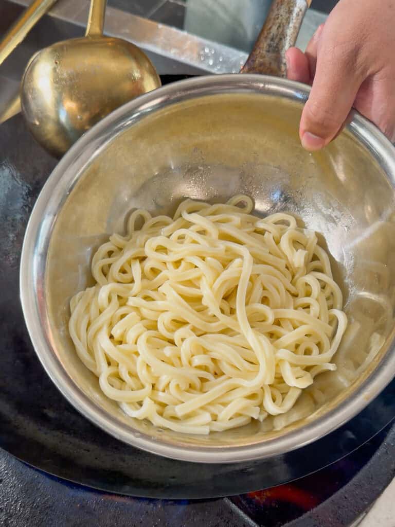 Fresh udon noodles added to wok with onions