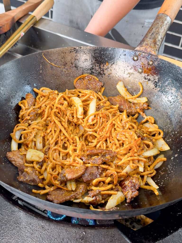 Onion slices and carrot strips added to bubbling wok.