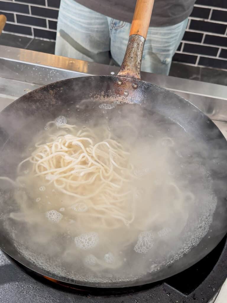 Shanghai noodles boiling in a wok with steam rising