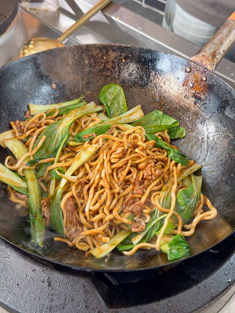 Tossing bok choy through Shanghai pork noodles until evenly combined