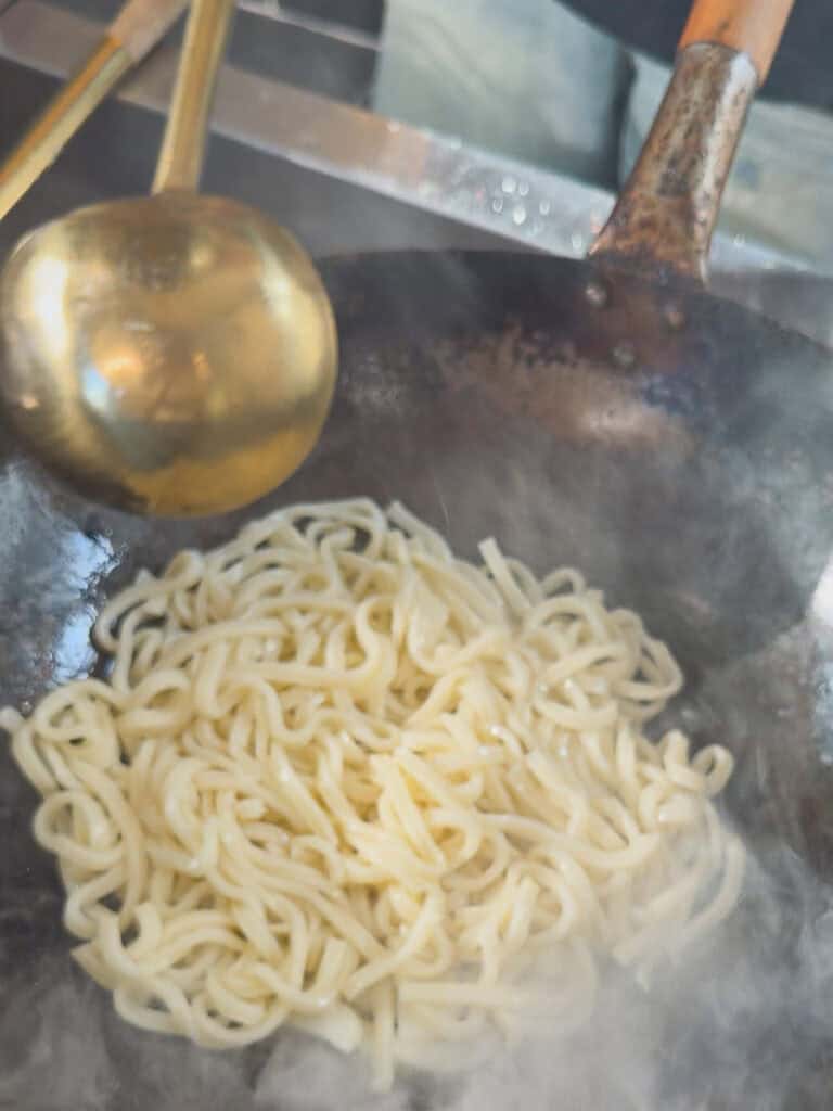 Udon noodles placed into hot wok for stir fry