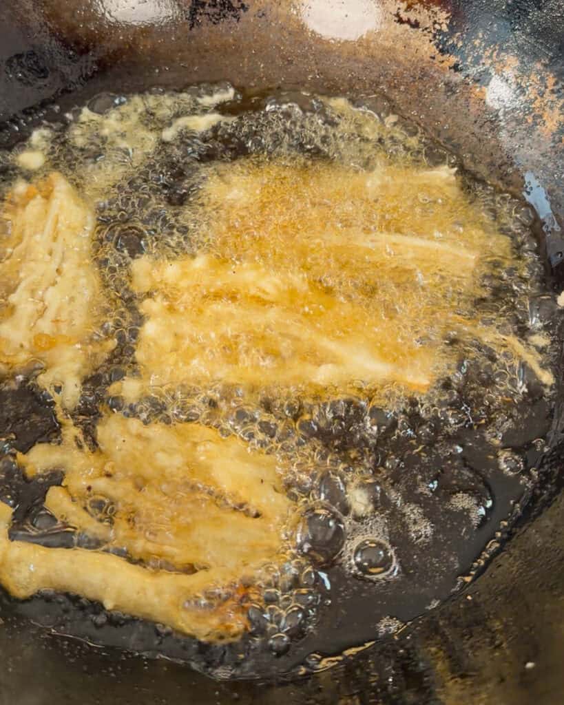 Enoki mushrooms frying in bubbling oil until golden