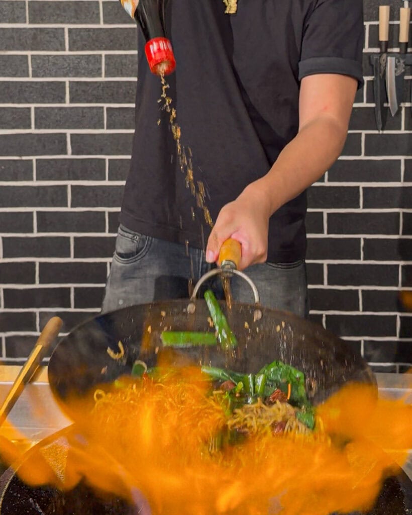 Final tossing of noodles and vegetables in wok
