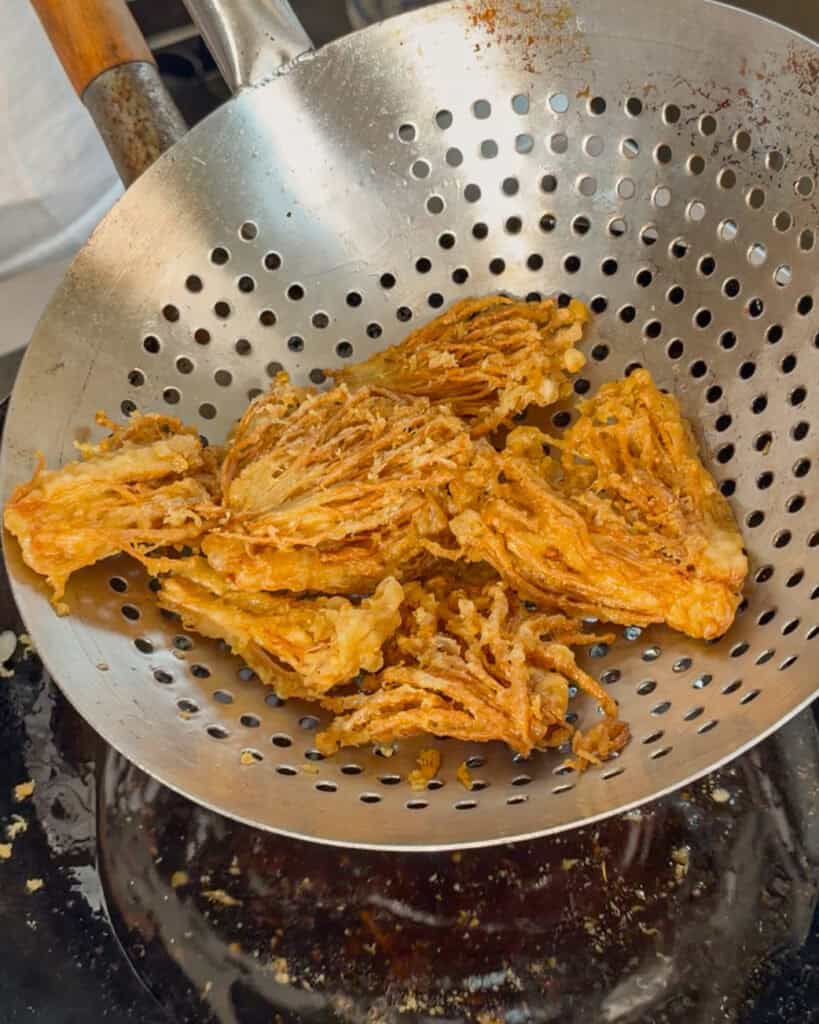 Fried enoki mushrooms draining in metal strainer