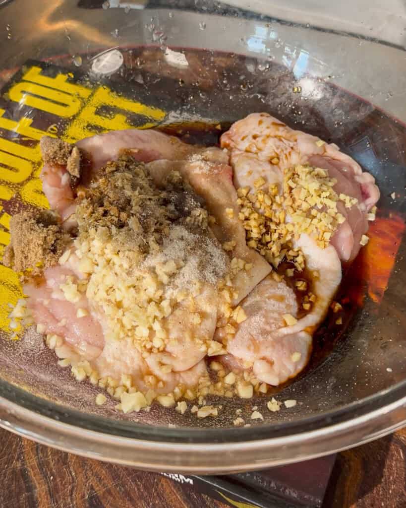 Garlic, chopped aromatics and sauces added to chicken in bowl