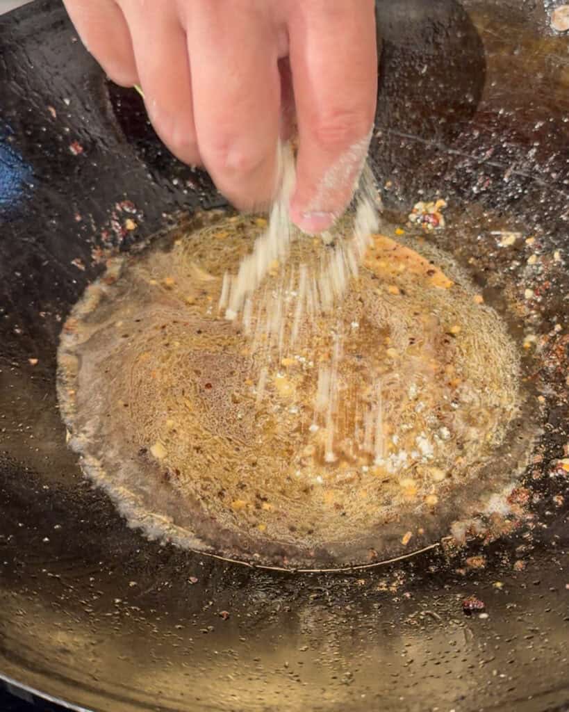 Granular seasoning being sprinkled into wok