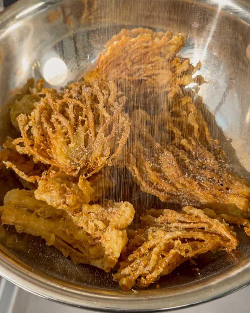 Shows fine seasoning being sprinkled over fried pieces in a bowl.