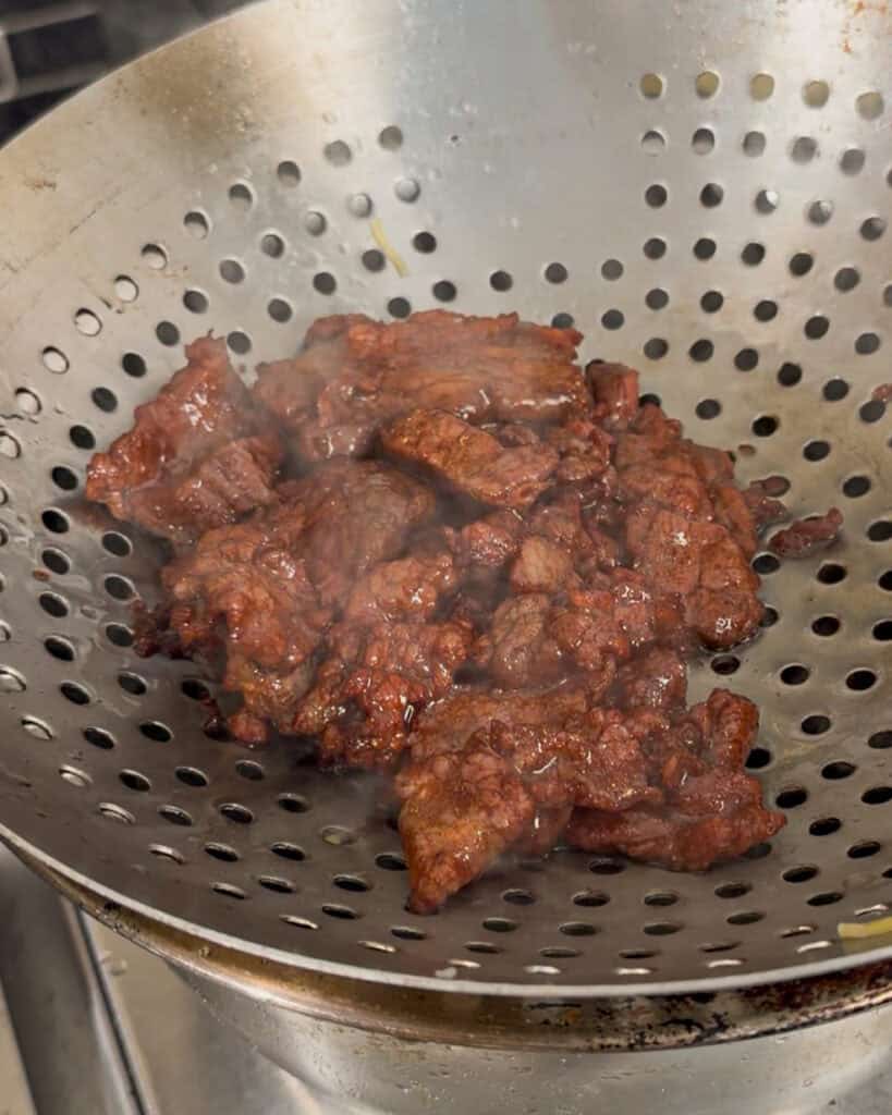 Straining cooked beef in a metal colander