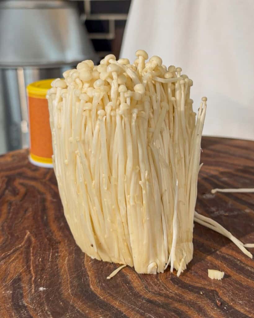 Whole enoki mushroom bundle placed upright on wooden surface
