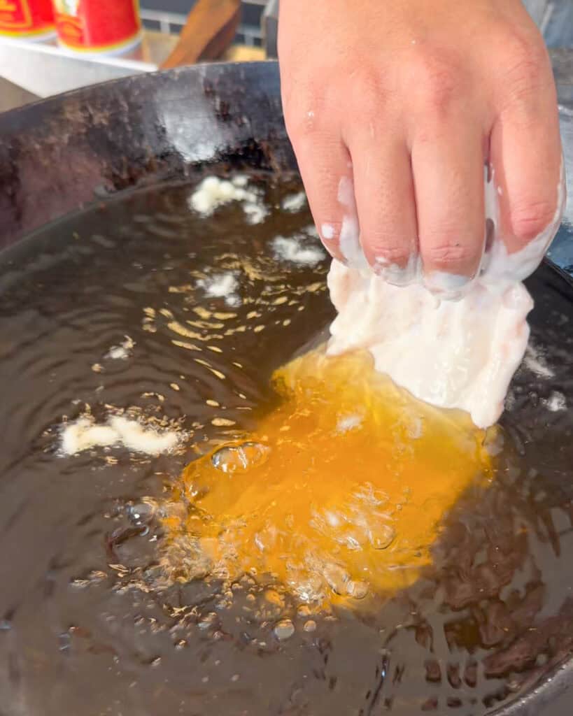Battered chicken piece being lowered into hot oil in a wok
