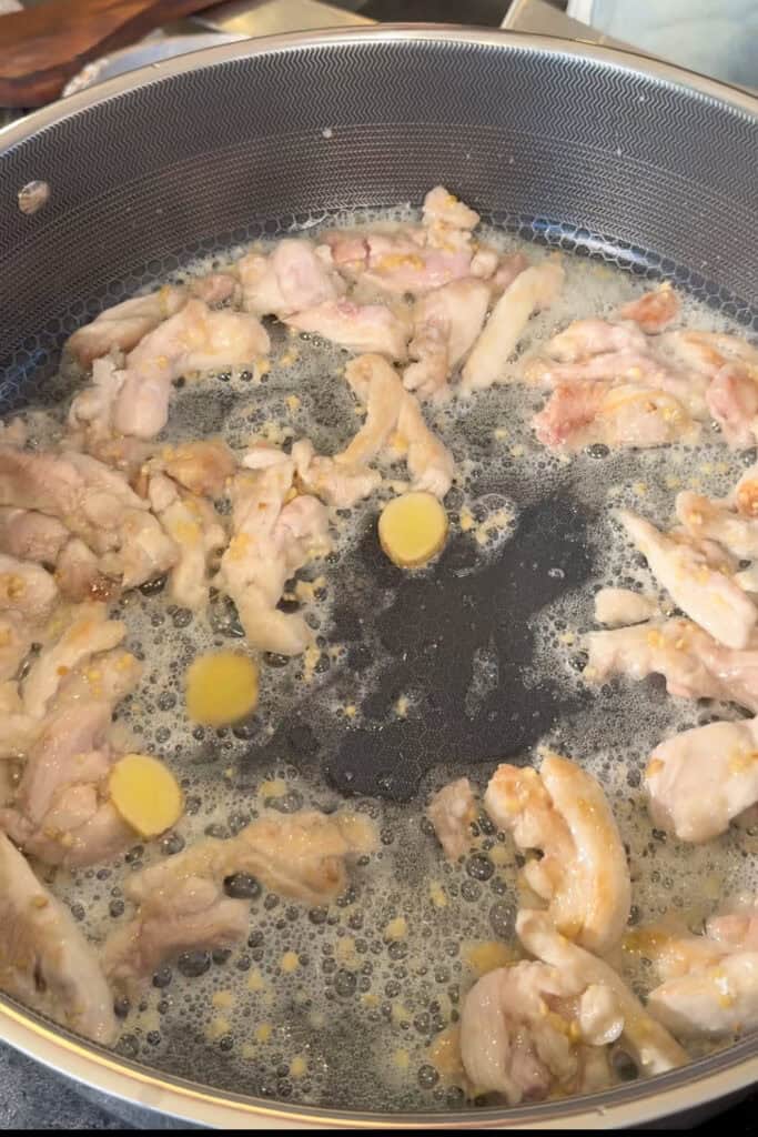 Chicken cooking with visible yellow slices and minced bits in a large pan