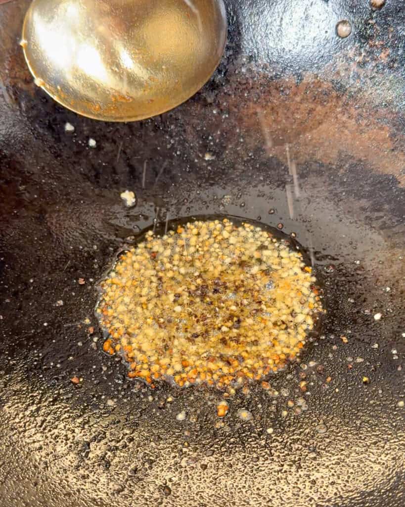 White flour mixture being added to marinated chicken pieces in a metal bowl.