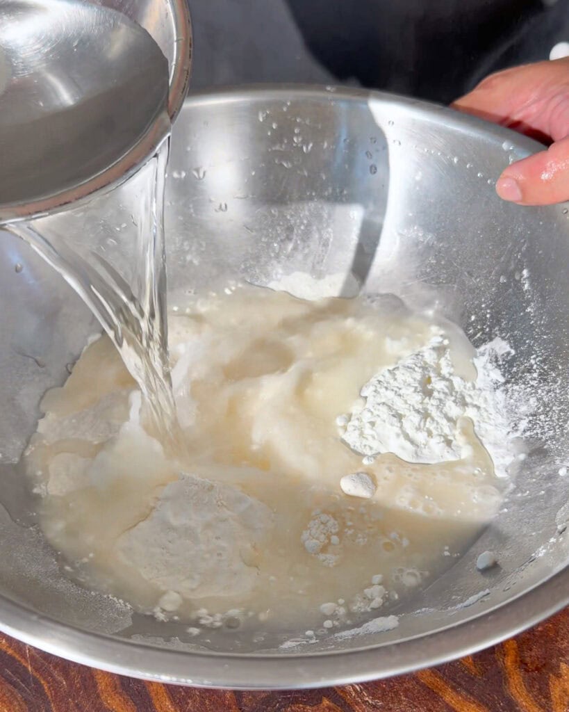 Clear liquid poured into white flour mixture in a metal bowl for chicken batter