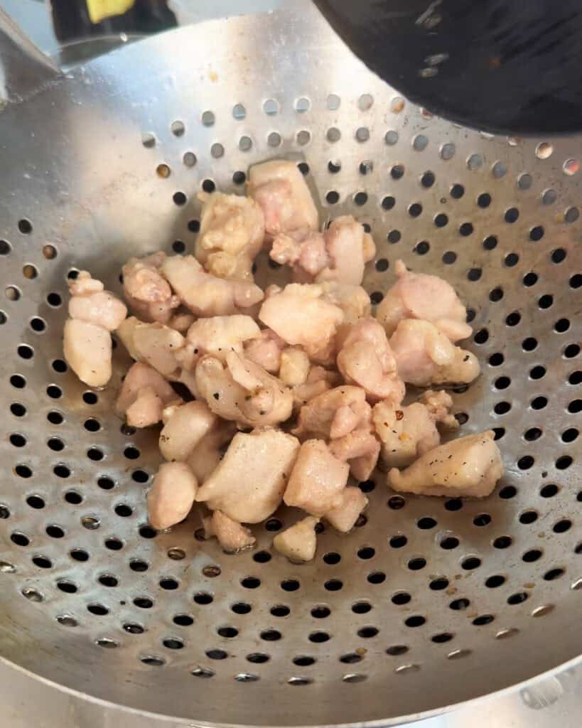 Cooked chicken pieces resting in a strainer for Kung Pao Chicken Noodles