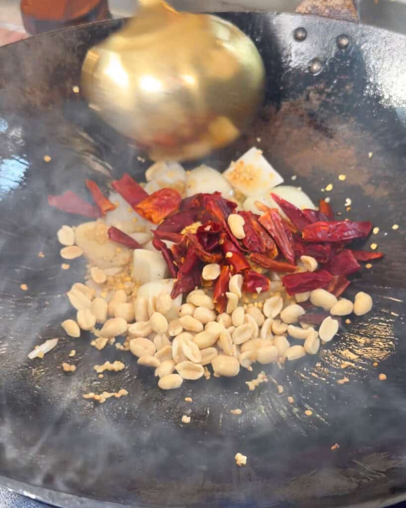 Dried red chillies peanuts onion and minced aromatics in a wok for Kung Pao Chicken Noodles
