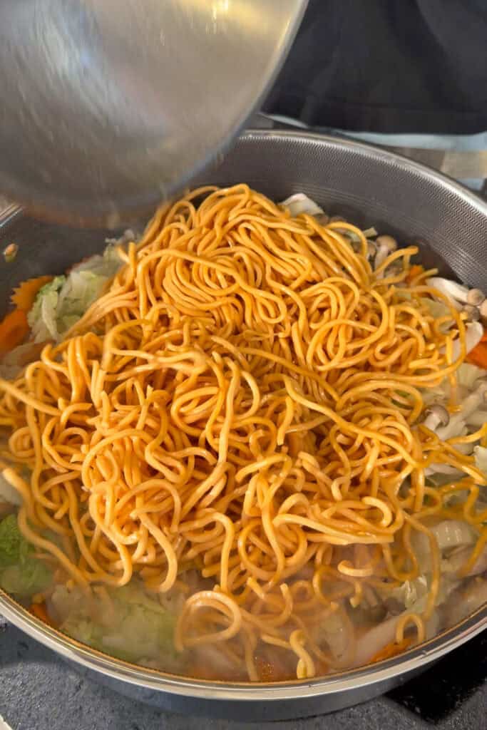 Egg noodles being added to a pan of vegetables