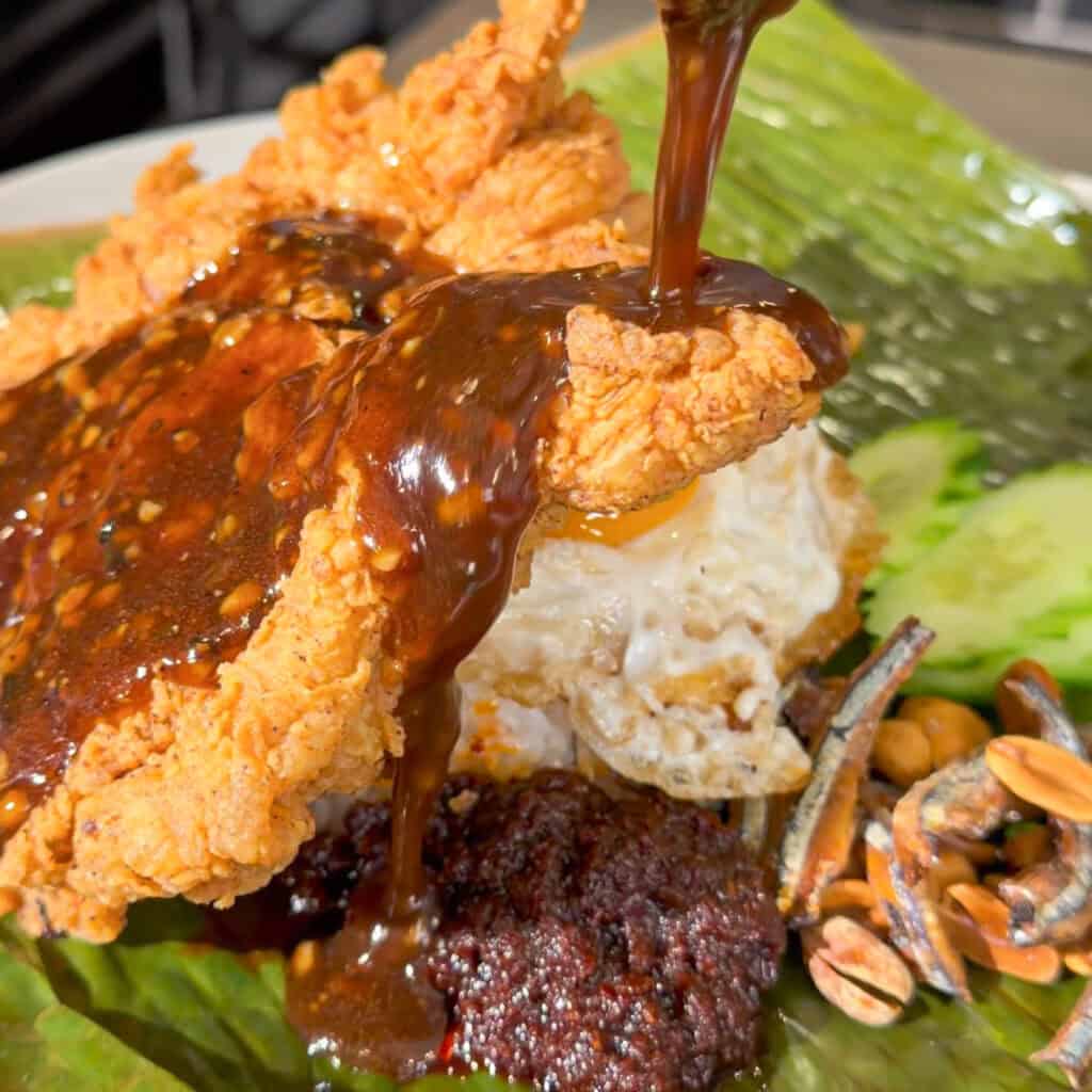 Thick glossy sauce being poured over crispy chicken on a plated rice dish.