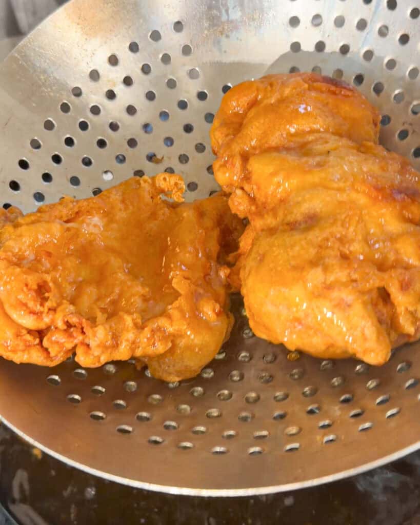 Golden fried chicken pieces resting in a perforated strainer after frying