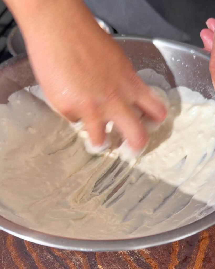 Hand mixing pale batter in a metal bowl for crispy chicken coating