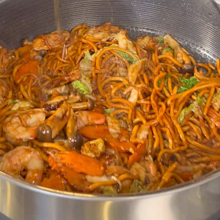 Liquid being poured over mixed noodles, shrimp, chicken, and vegetable