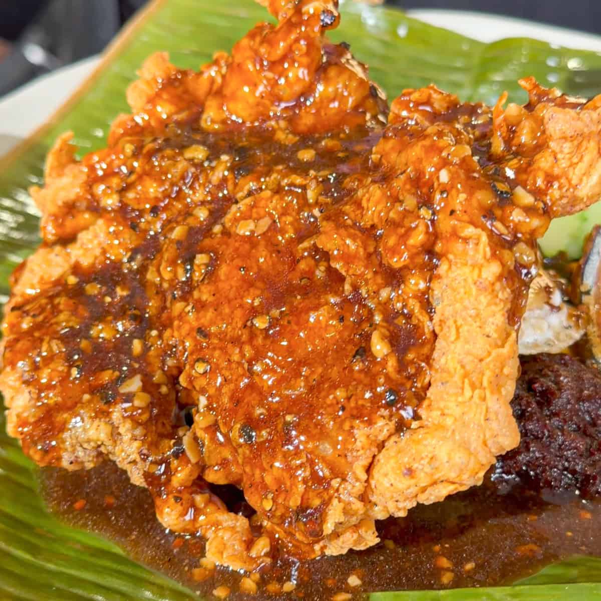Crispy fried chicken coated in spicy sauce with sesame seeds on a banana leaf plate