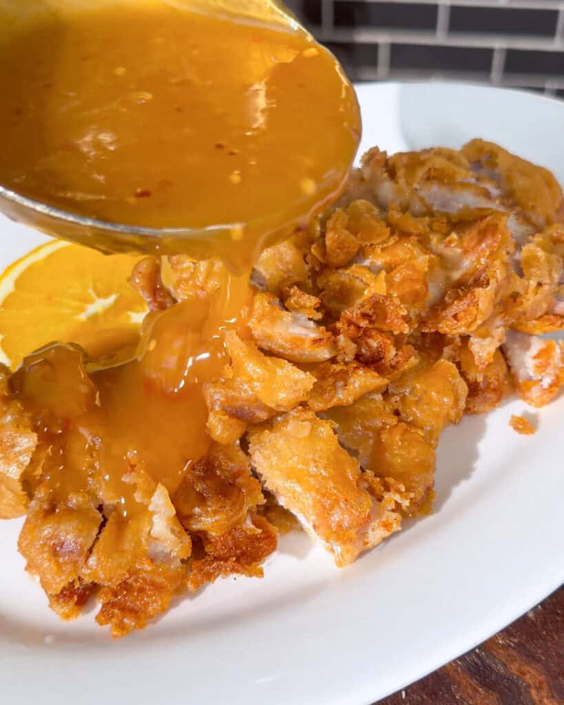 Orange sauce poured over chopped crispy fried chicken on a white plate