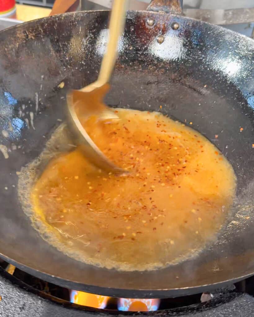 Orange sauce with chili flakes being stirred in a wok