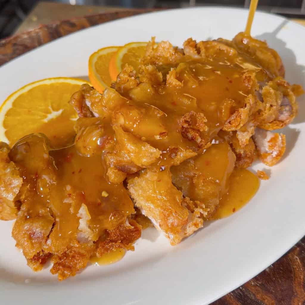 Plated crispy chicken covered with glossy orange sauce and orange slices
