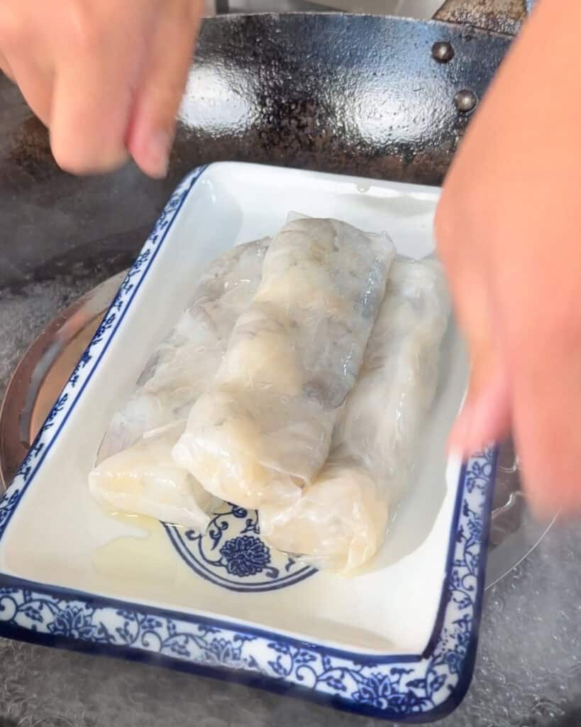 Several pale dumplings wrapped in plastic sit in a blue-and-white ceramic dish on a kitchen counter.