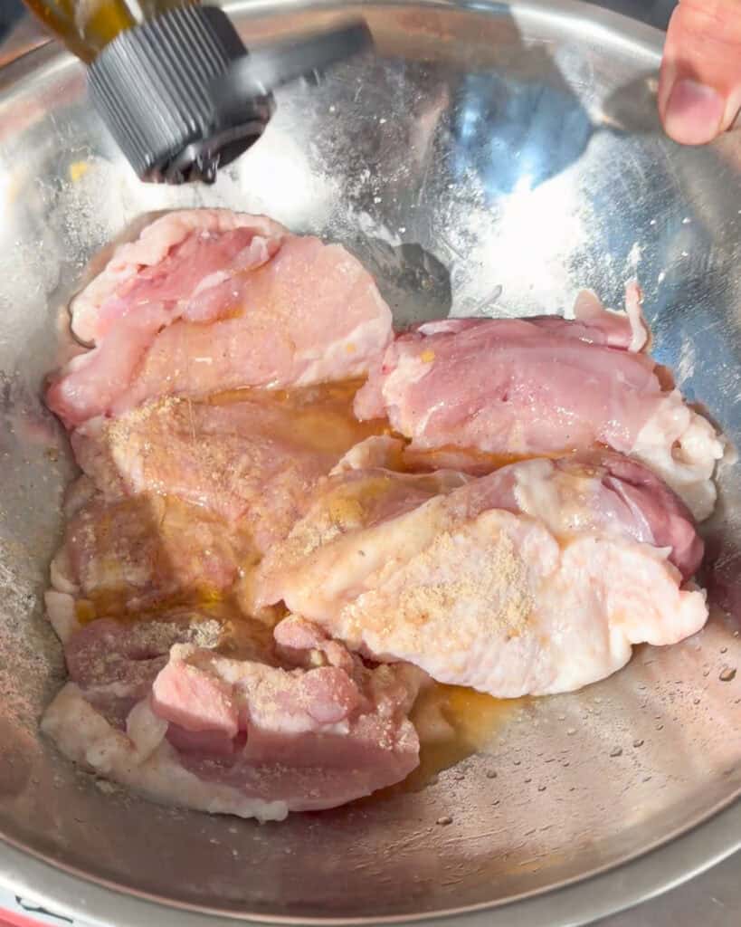 Raw chicken thighs being mixed in a metal bowl with a visible coating
