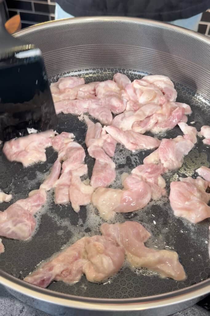 Sliced chicken cooking in a large pan