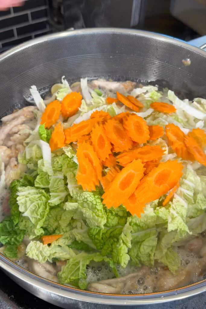 Wombok cabbage and sliced carrots added to chicken in a pan