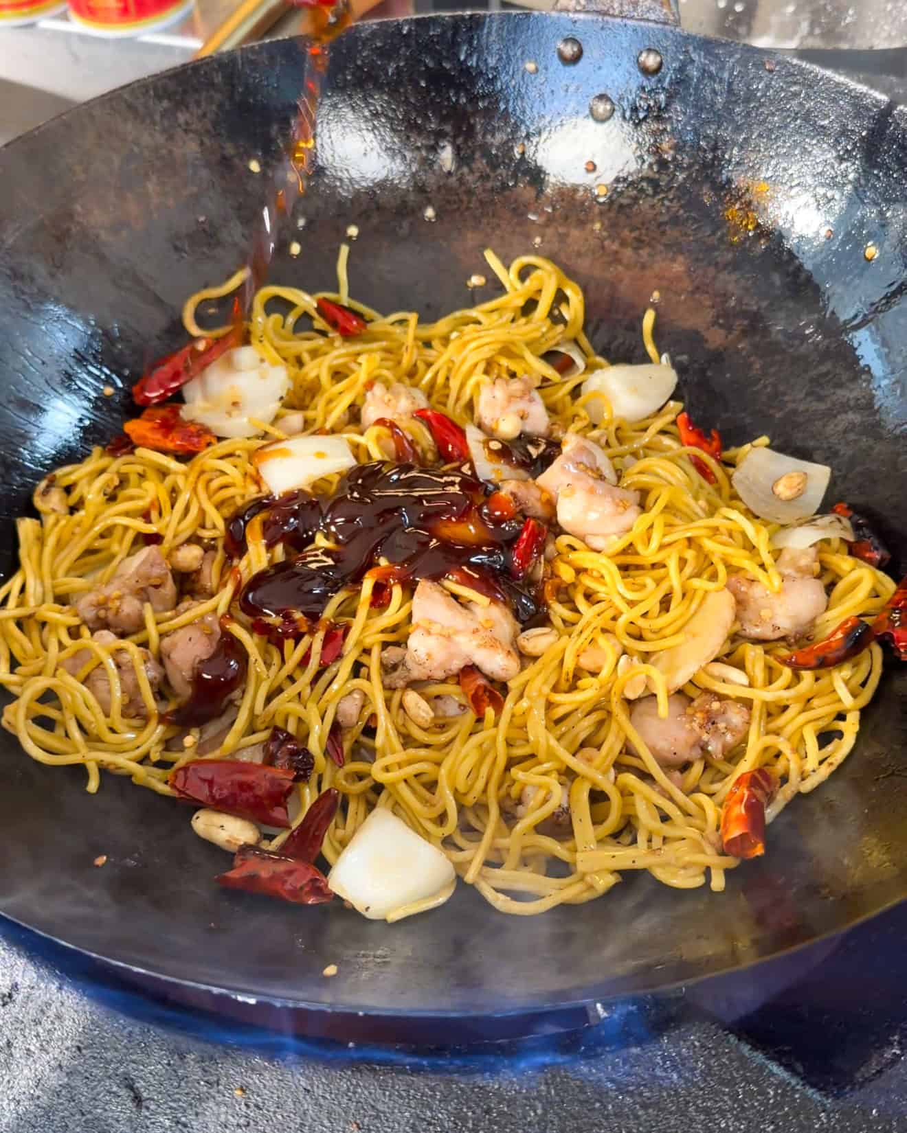 Yellow noodles mixed with chicken chillies peanuts and onion in a wok