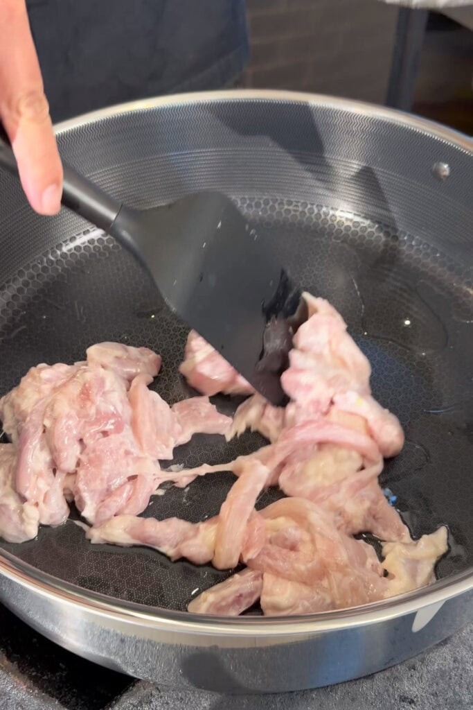 sliced chicken being stirred in a large pan with oil.