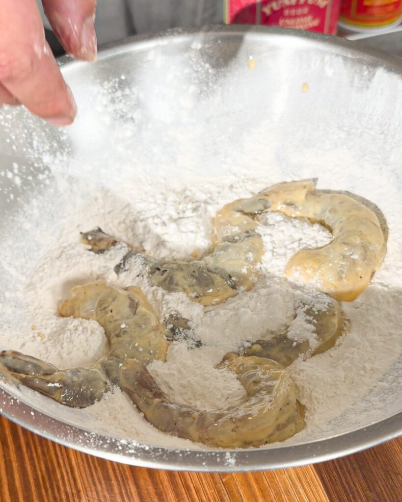 Coated king prawns being covered in flour before frying