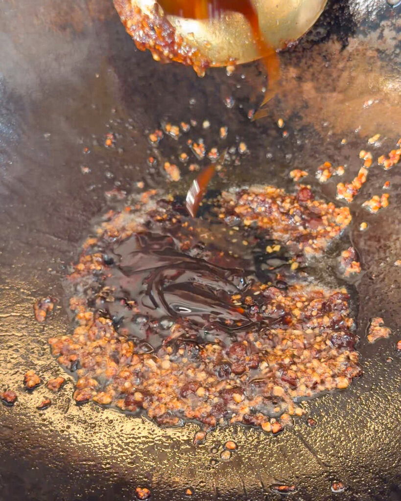 Dark glossy sauce poured into a wok while building sauce
