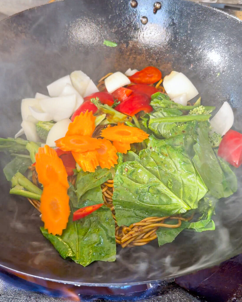 Noodles with broccoli, greens, onion, capsicum, and carrot in a wok