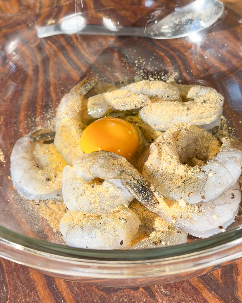 Raw king prawns with seasoning powder and egg in a glass bowl