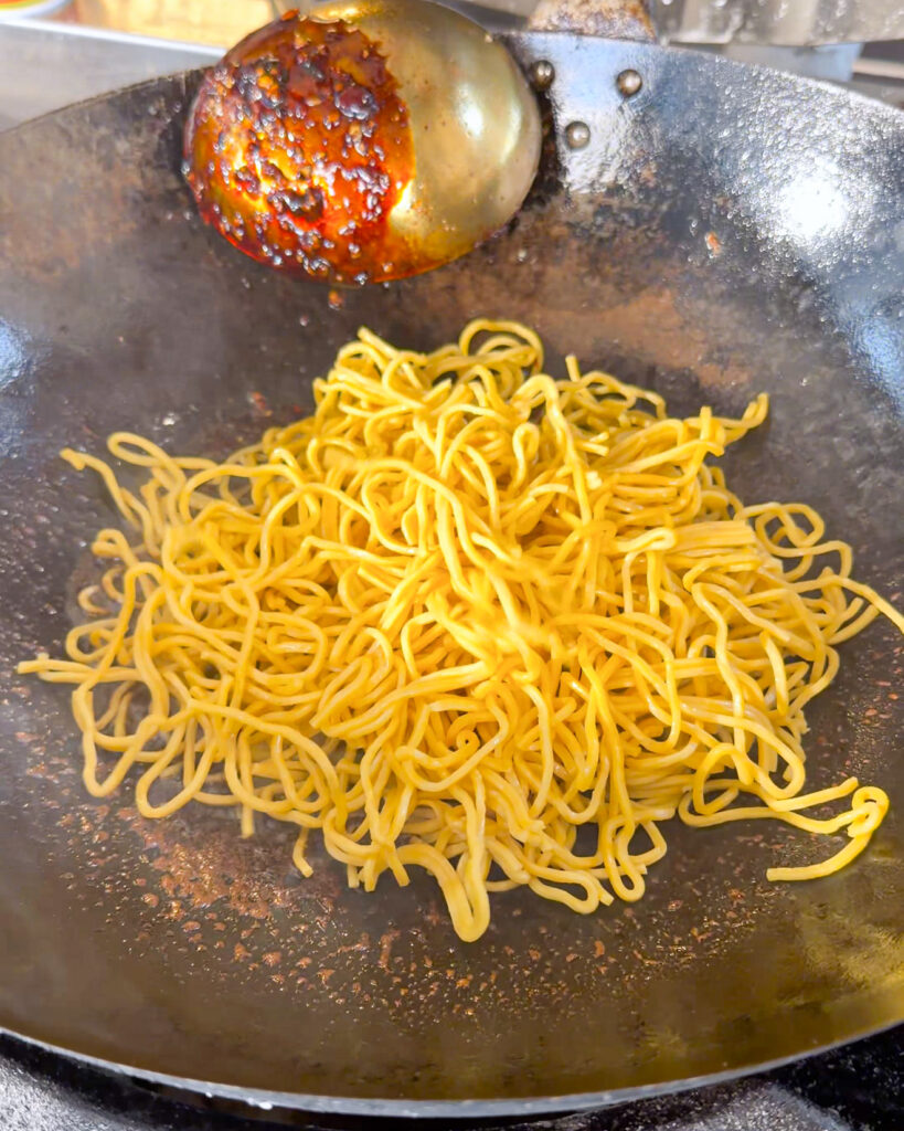 Yellow noodles added to a wok with sauce